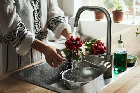 A woman standing by the sink rinsing a bunch of radishes using the ÄLMAREN kitchen tap