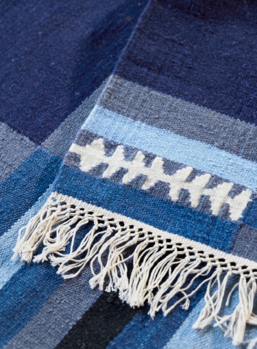 A close-up of a handmade striped TRANGET wool rug in white, black, grey and different blue colours.