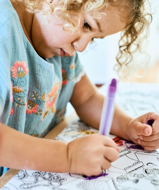 A small child colouring in an illustration with a purple crayon.