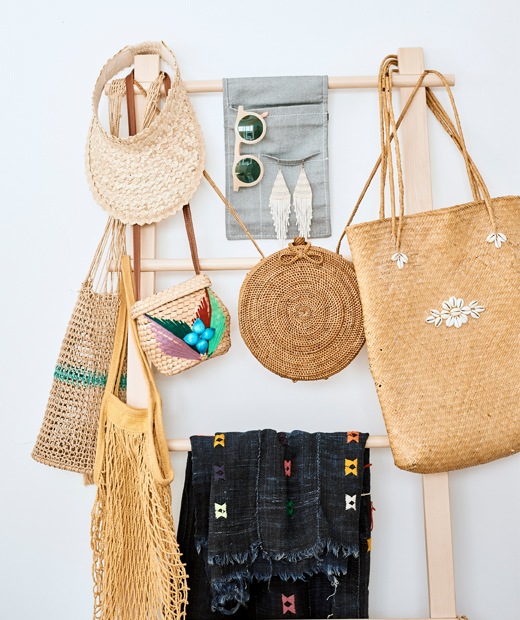 Rattan handbags and accessories hanging on a wooden ladder stand.