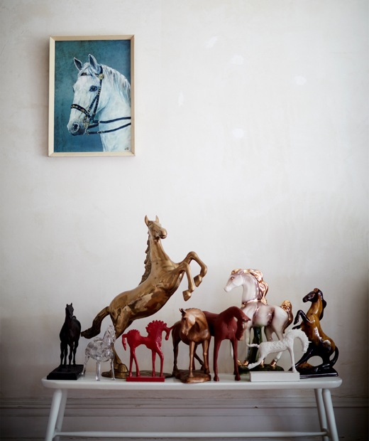 A collection of horse ornaments on a white bench and a painting of a horse on the wall above.