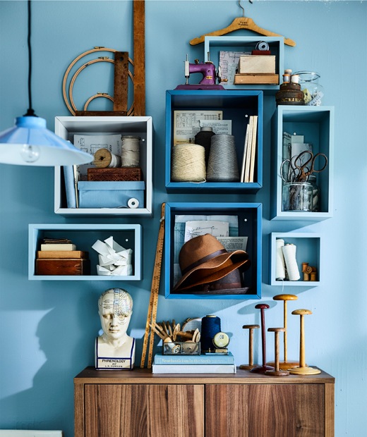 Sewing equipment and books stored in white cubed units on a blue wall.
