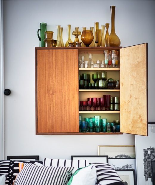 Glass vases stored inside and on top of a wall-mounted cabinet, grouped by colour.