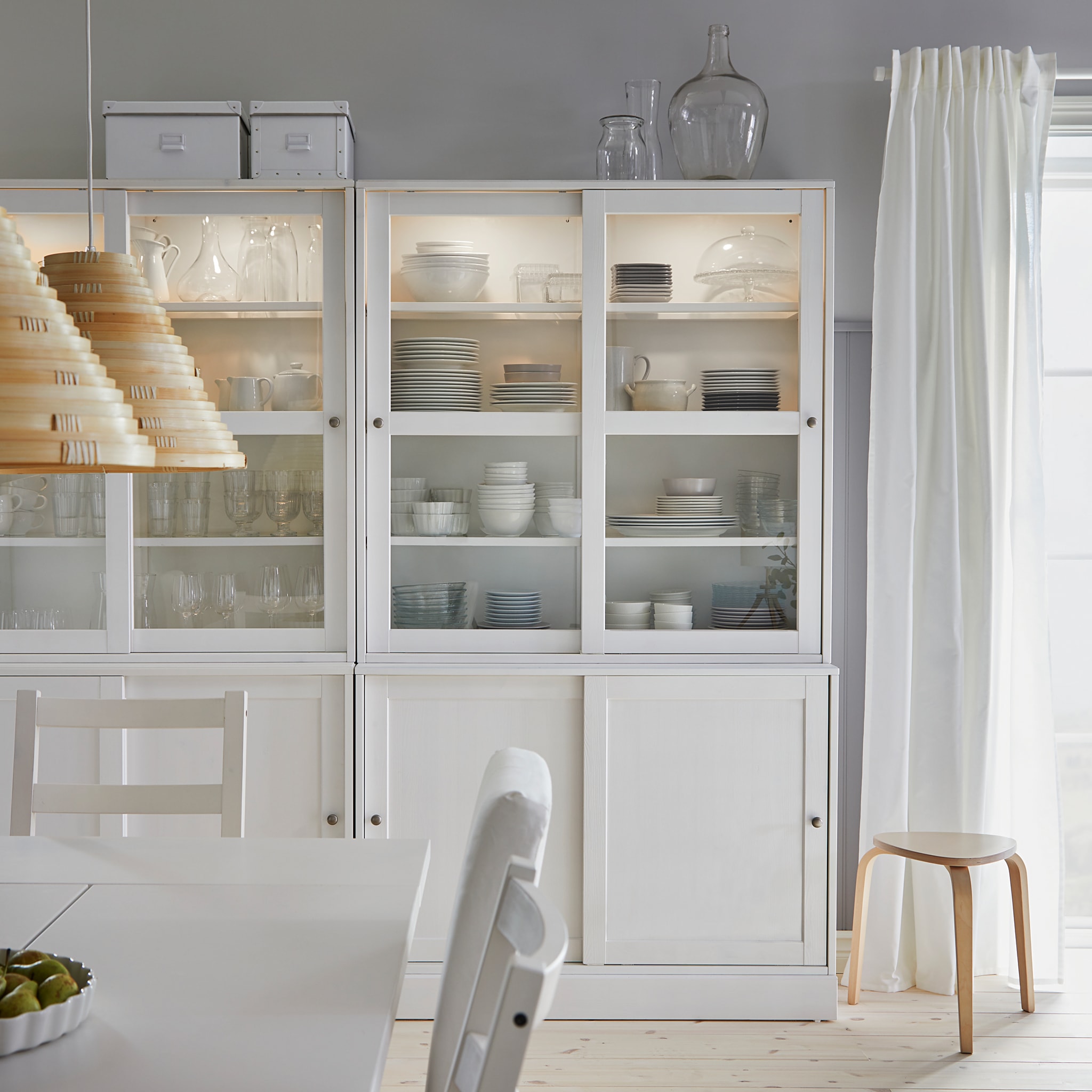  A HAVSTA white storage combination with sliding glass doors store dinnerware and glasses in a dining room.