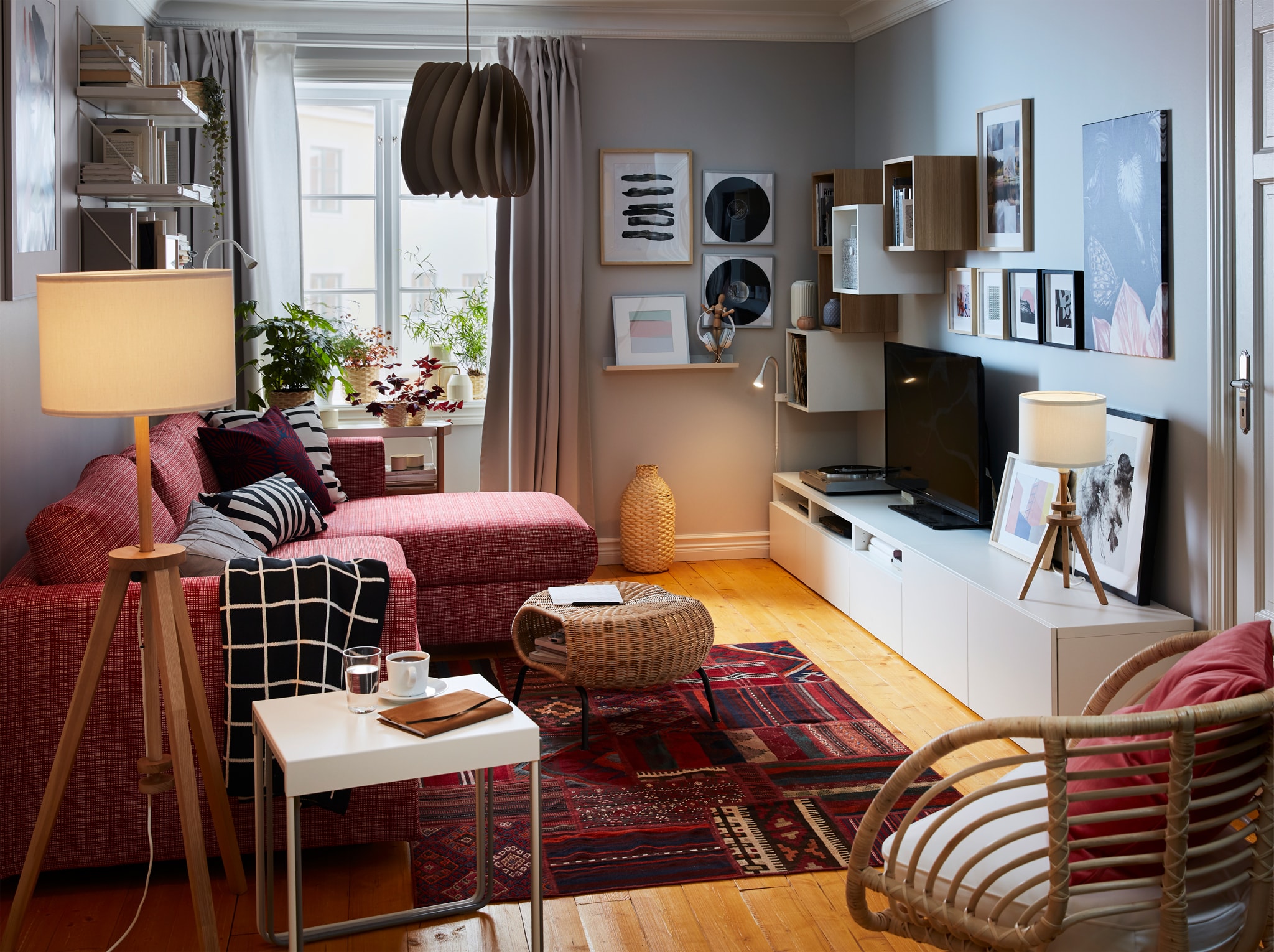  A small living room with a red Persian patterned rug, a red sofa, grey curtains, an armchair in rattan and mood lighting.