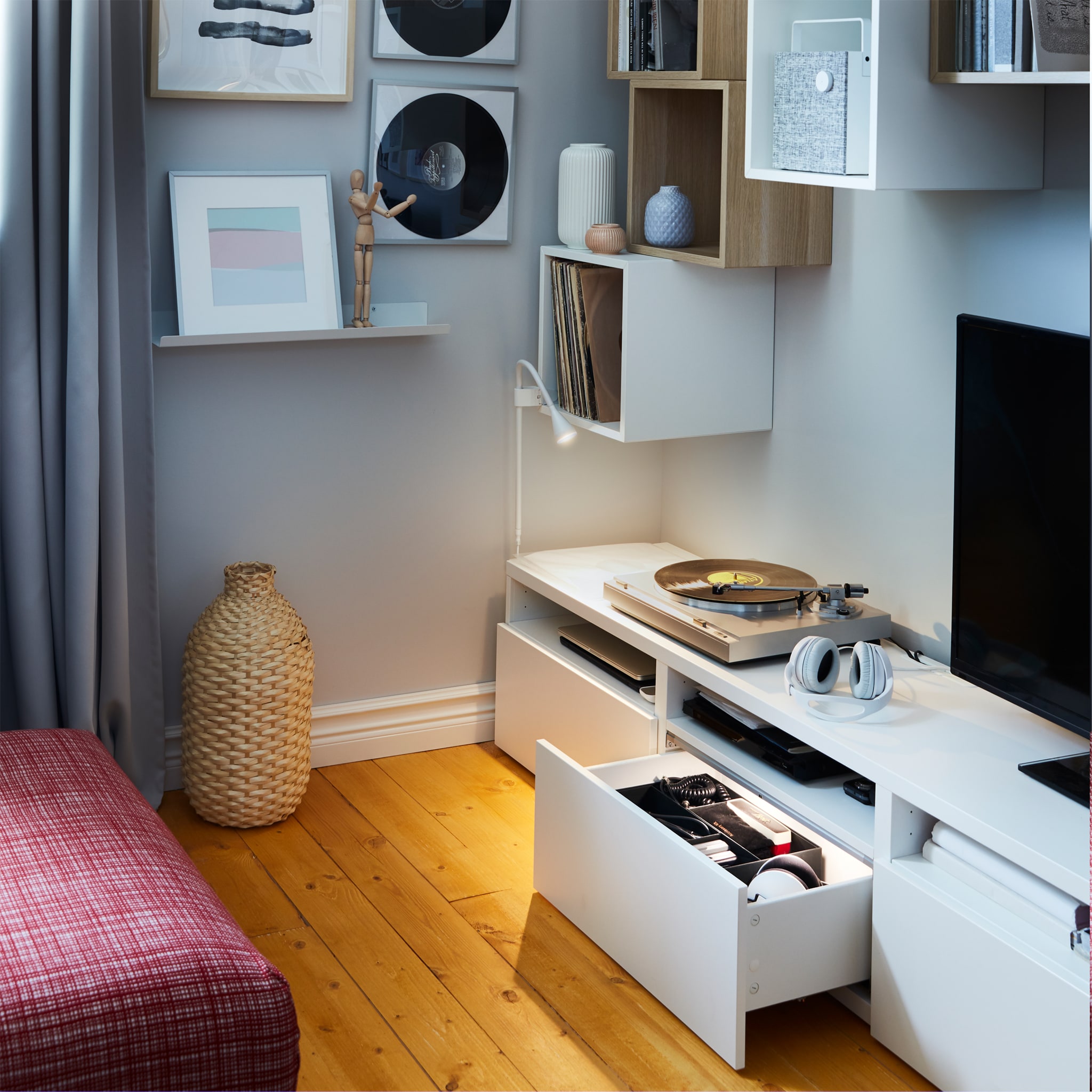  A white TV bench with an open and illuminated drawer, white wall cabinets, a small wall lamp and a decoration vase in bamboo.