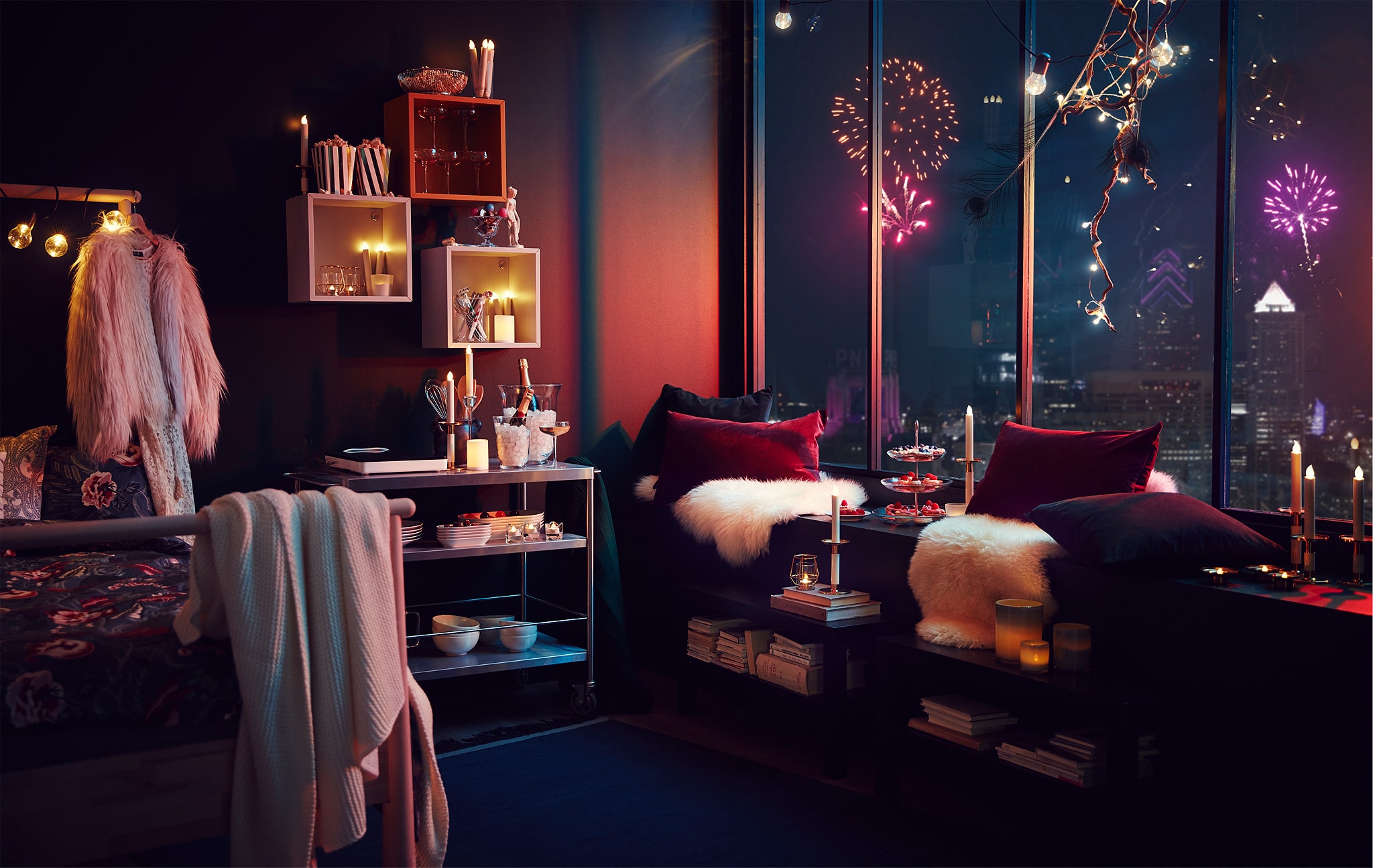 Interior apartemen dengan dekorasi pesta dan lampu; kembang api dari kota terlihat melalui jendela tinggi.