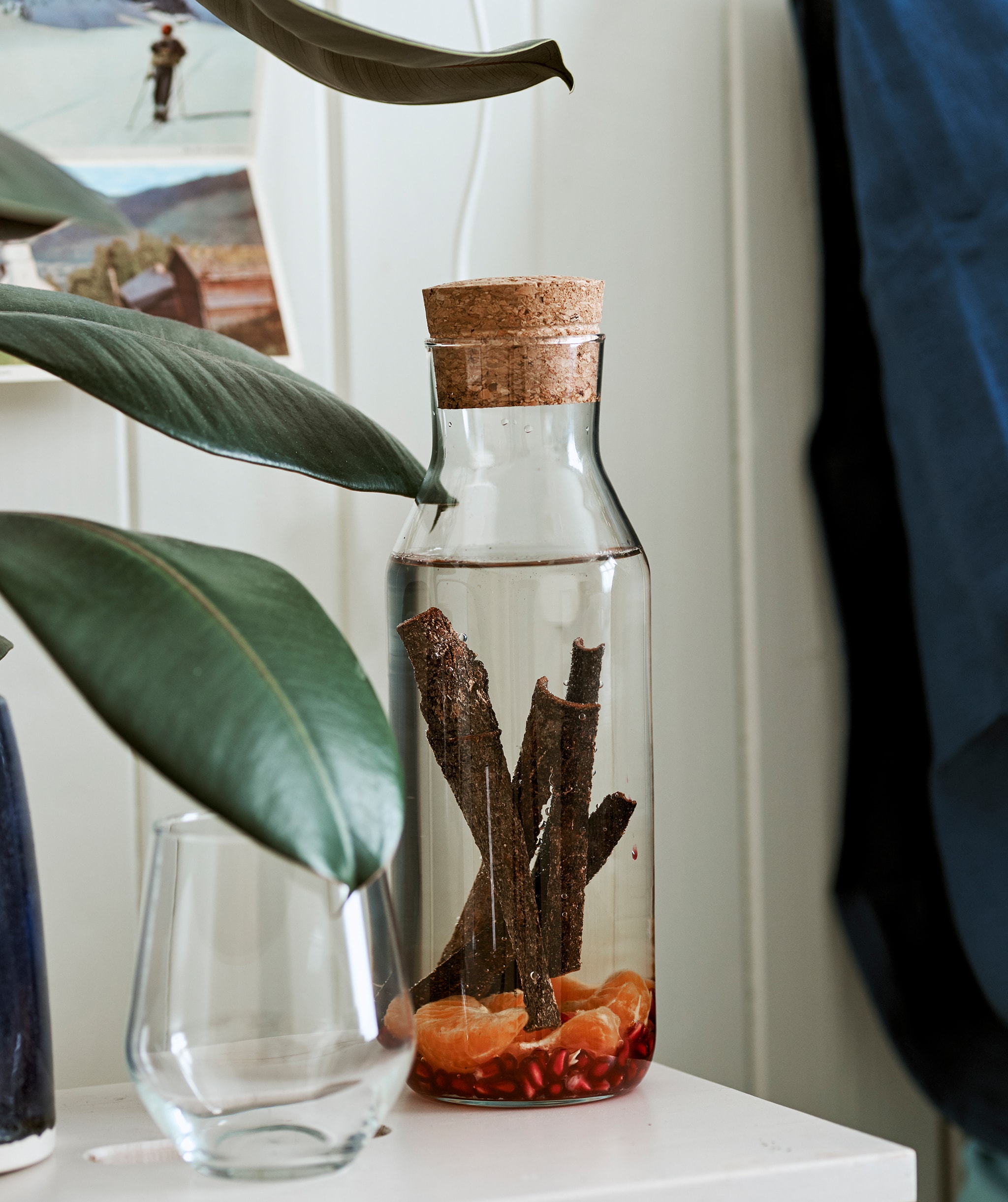 A glass carafe with cork stopper filled with water infusing with cinnamon sticks and fruit, next to a drinking glass.
