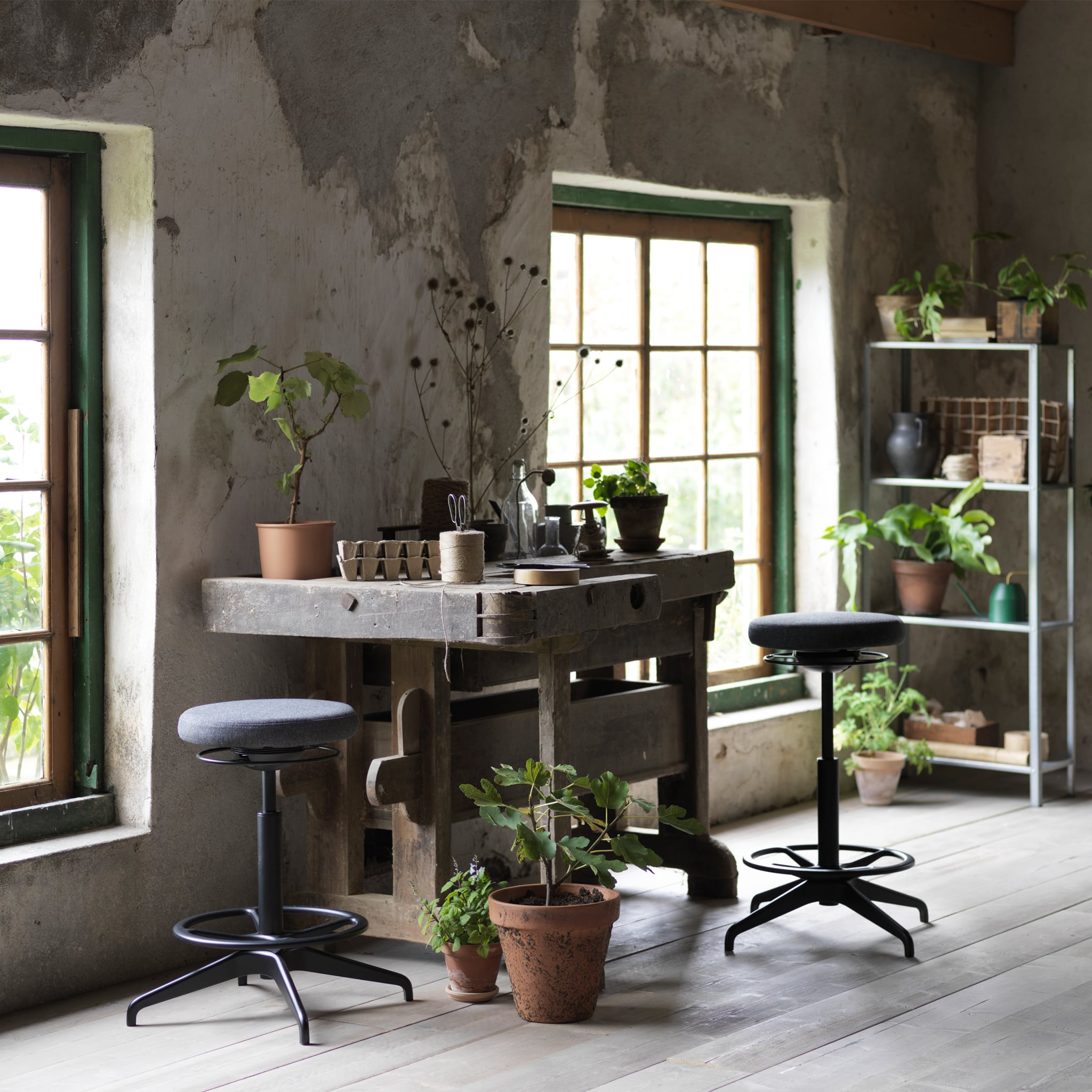 Two LIDKULLEN active sit/stand supports in dark grey placed in a gardener’s workspace surrounded with plants.