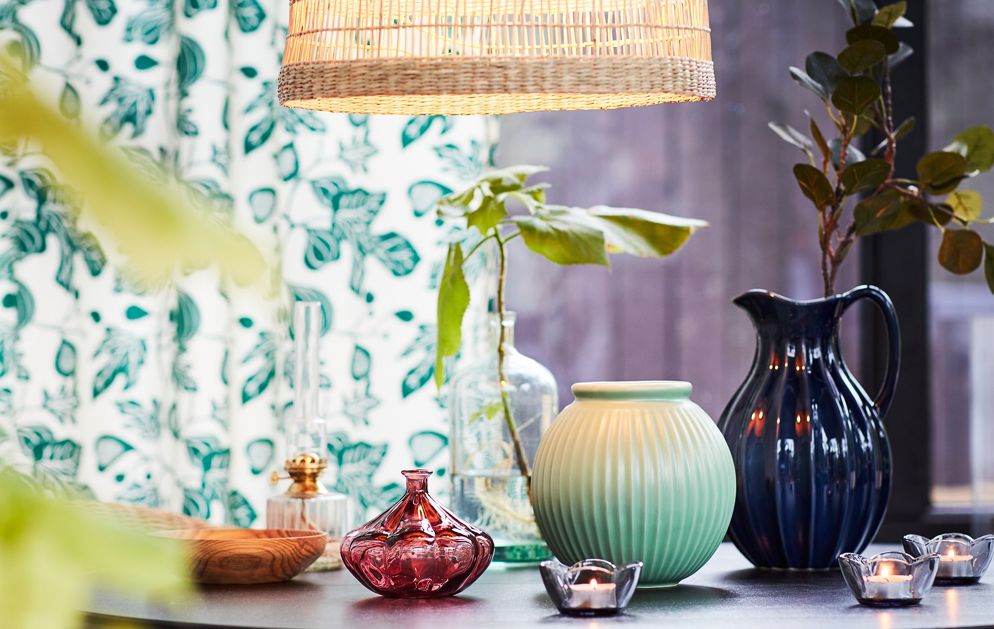 Sebuah meja yang dihiasi dengan vas kecil dan lilin dengan sedikit daun hijau dan penanda musim semi.