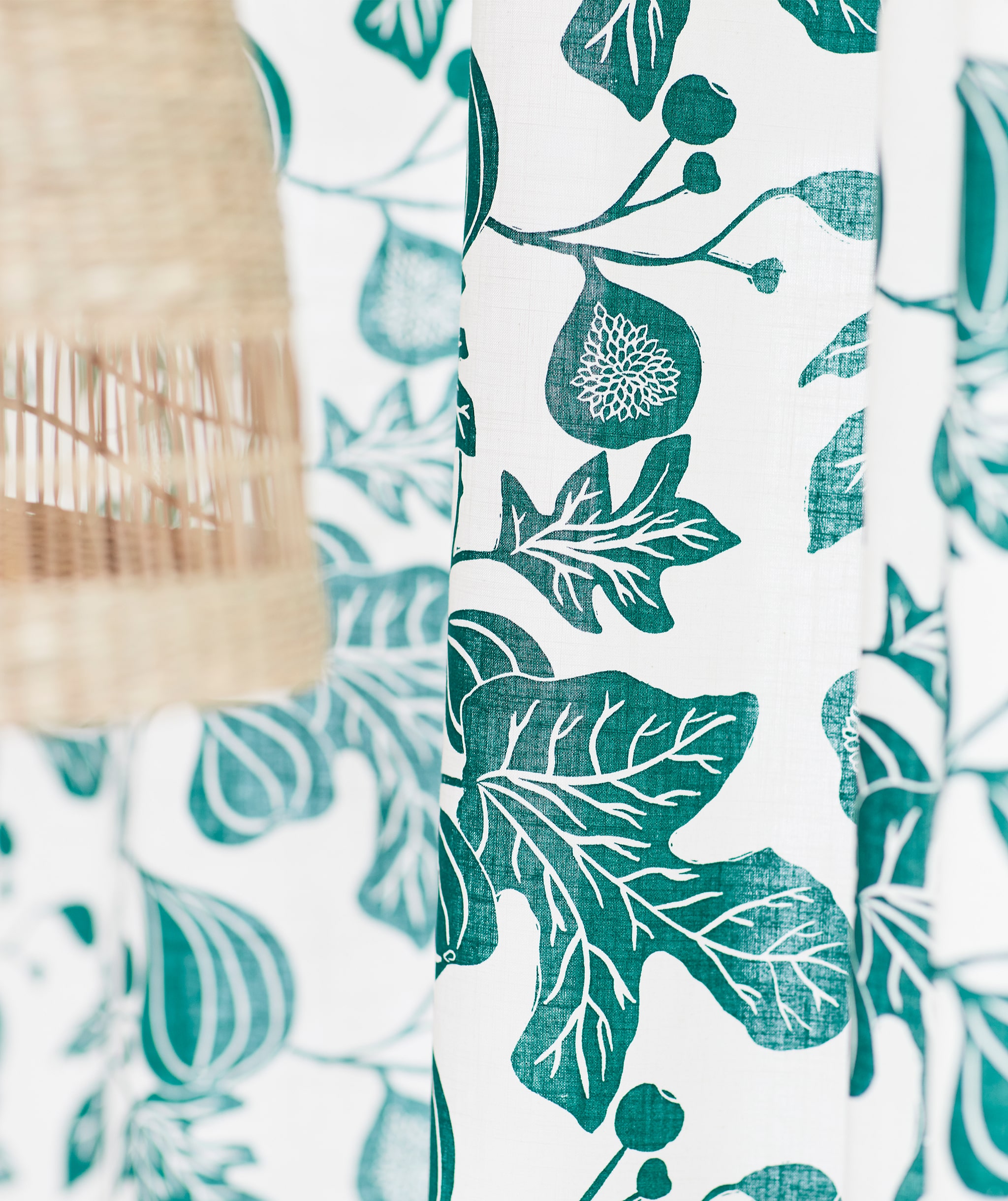 Tirai putih dengan pola ranting pohon ara warna hijau, berada di sebelah lampu plafon yang terbuat dari serat pisang alami.