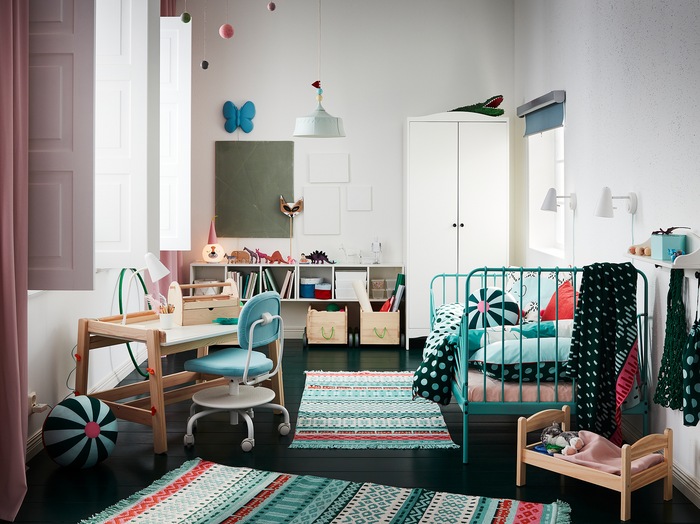 A children’s room with colourful rugs, a bed frame in turquoise, a white wardrobe, pink curtains and a children’s desk.