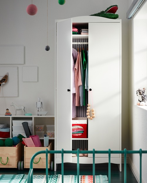 A children’s room with a wardrobe with one door that’s open. Boxes and both hanging and folded clothes are stored inside.