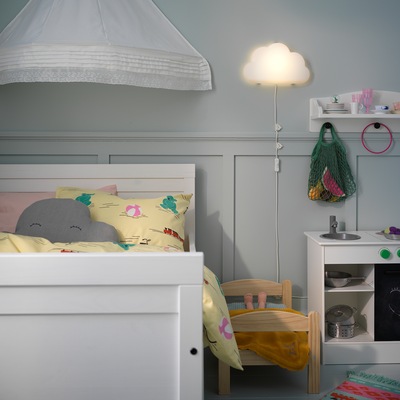 Wall-mounted UPPLYST LED wall-lamp is shaped like a cloud and gives a cosy light next to a white children’s bed.