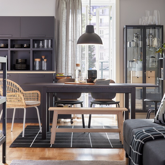 A dining room with an extendable table that’s extended. Black chairs, a rattan chair and a bench in birch provide seating.