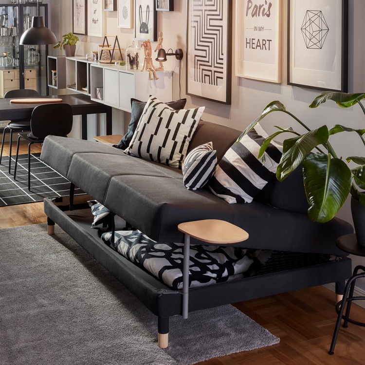 A dark grey FLOTTEBO sofa-bed where the seat has been lifted, underneath it is storage space with a duvet and a pillow.