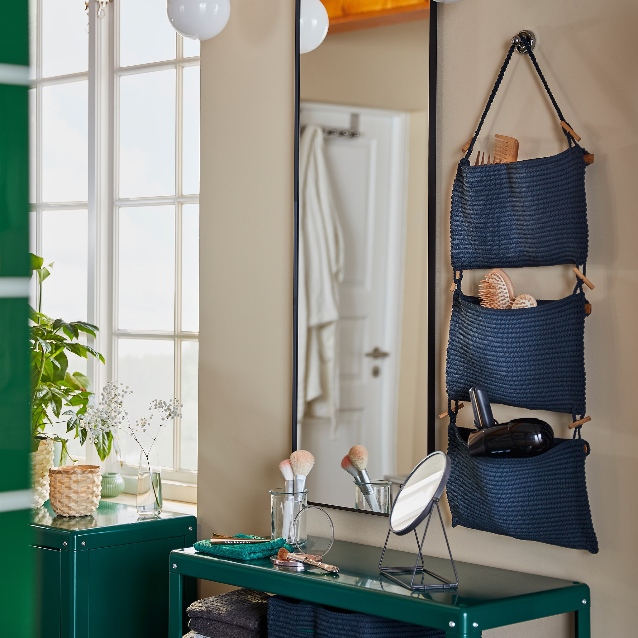 A bathroom beauty station that consists of NORDRANA hanging storage, a wall-mounted mirror and a green shelving unit.