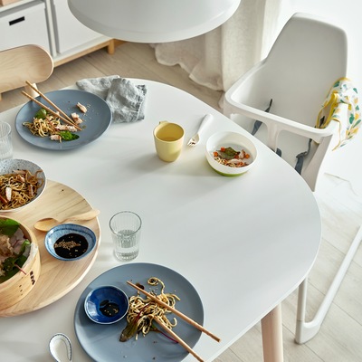 A white dining table with leftovers from a family dinner. Next to the table is a white highchair.