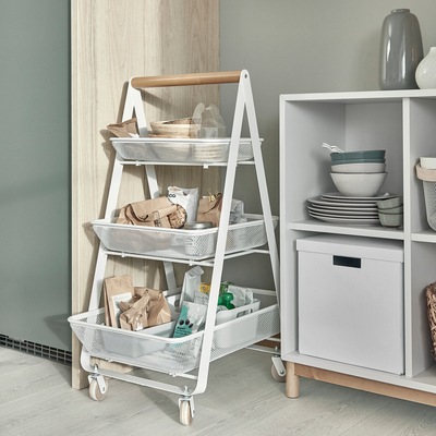 A trolley on castors with three steel mesh baskets where snacks, dry goods and bowls are stored. It stands next to a cabinet.