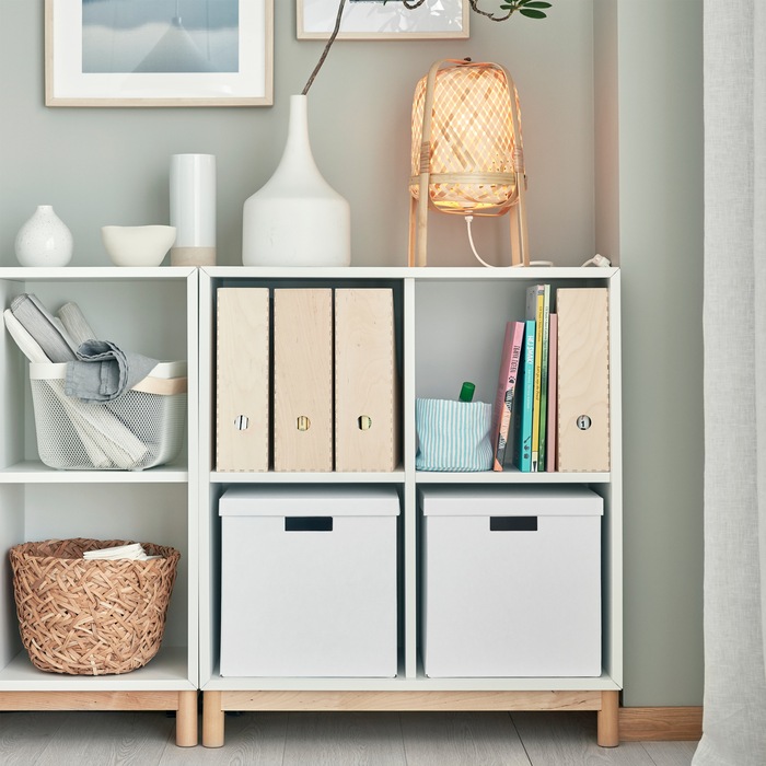 A white EKET cabinet combination with legs in birch. Different storage boxes and decorations stand on the shelves and on top.