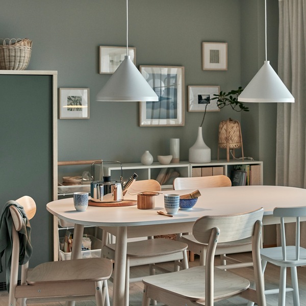 Tea for two is served on a dining table. Two lit NÄVLINGE pendant lamps are above, and they give a cosy, dimmed lighting.