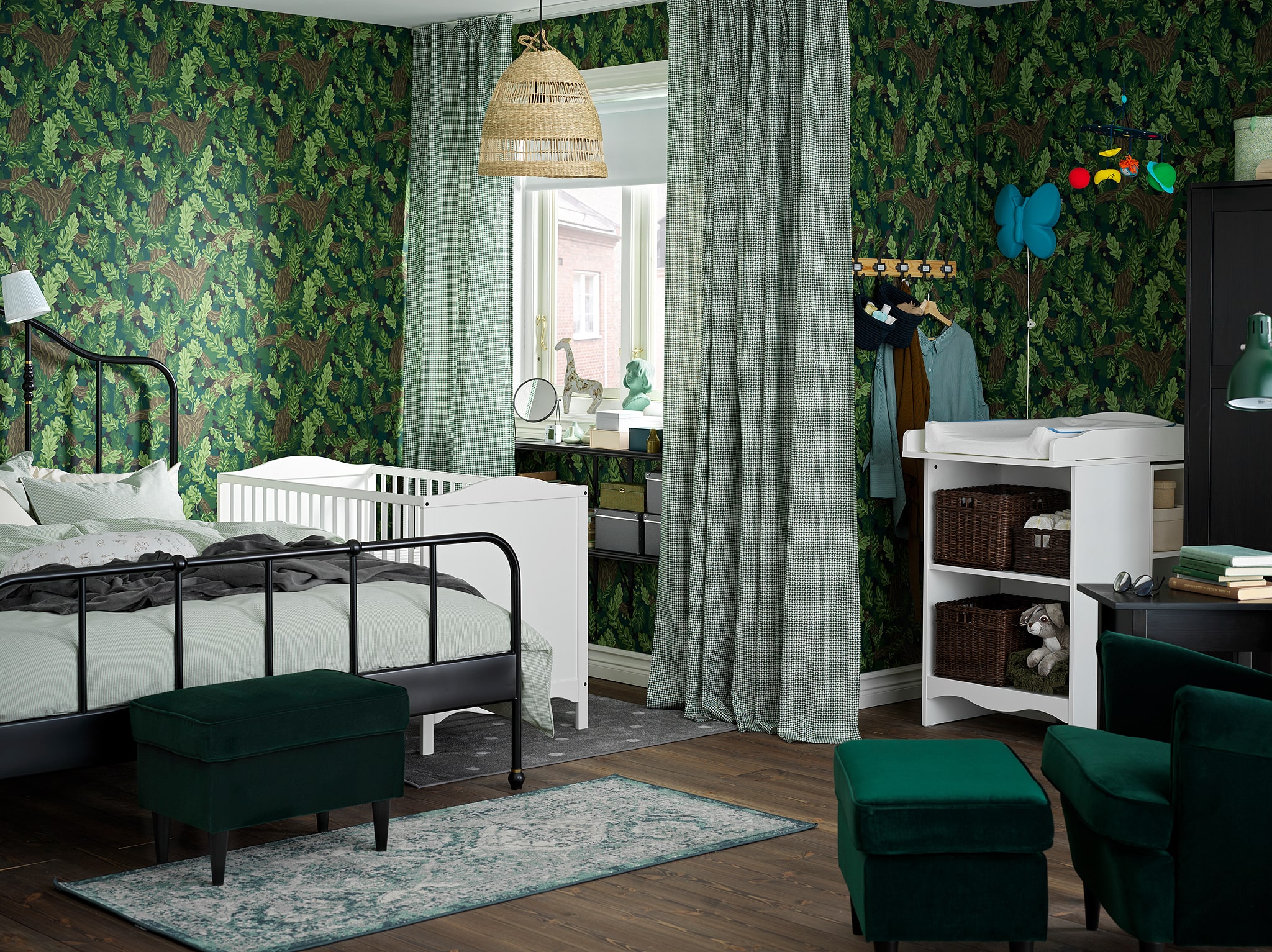 An overall green bedroom/children’s room with a changing table and cot in white, a black bed frame and white/green curtains.