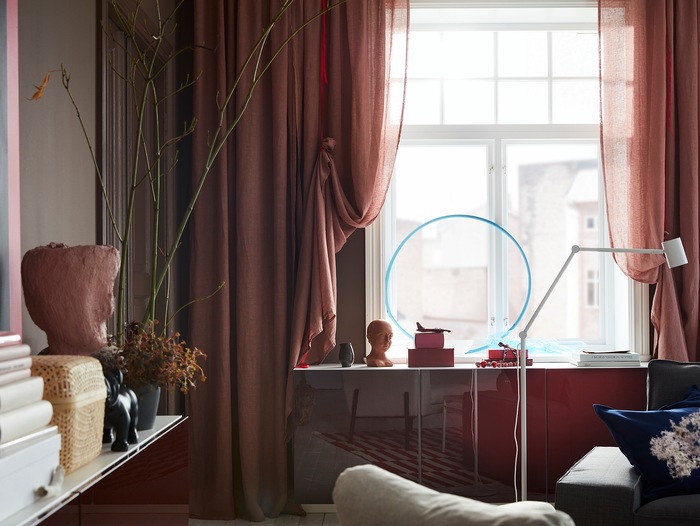 Light brown-pink LEJONGAP curtains are draped with red ribbons and hang by a window where the light shines in beautifully.