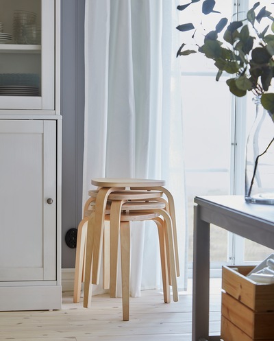 Empat kursi KYRRE dengan material kayu birch ditumpuk di dekat jendela, dan kursi-kursi tersebut menyediakan tempat duduk tambahan untuk meja makan saat diperpanjang.