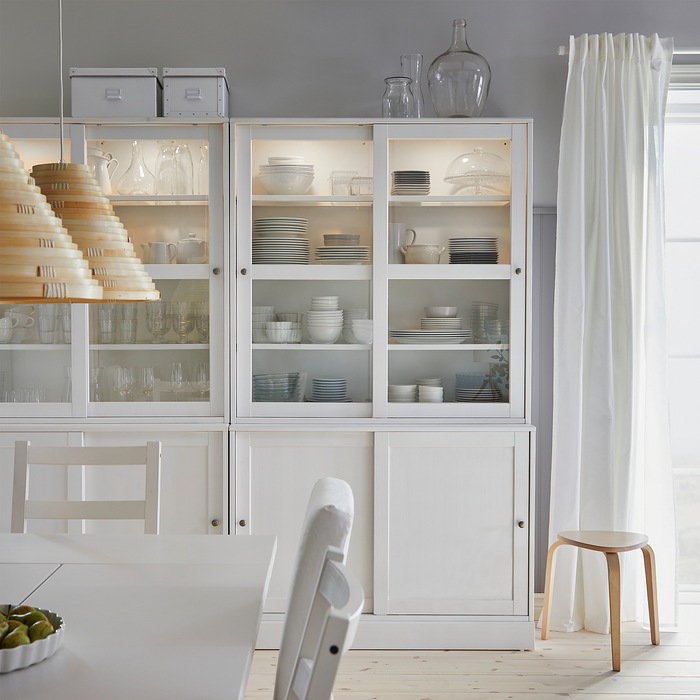 A dining room where dinnerware and glasses are stored inside a white HAVSTA storage combination with sliding glass doors.