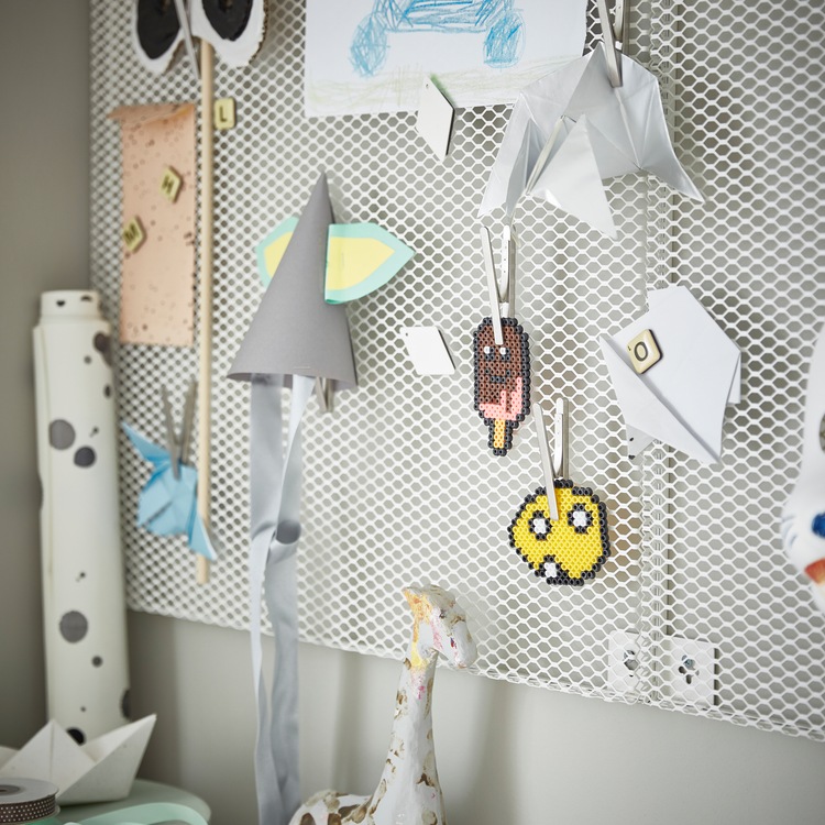 A white, wall-mounted SÖDERGARN memo board with magnets and clips, and attached on them are children’s crafts and drawings.