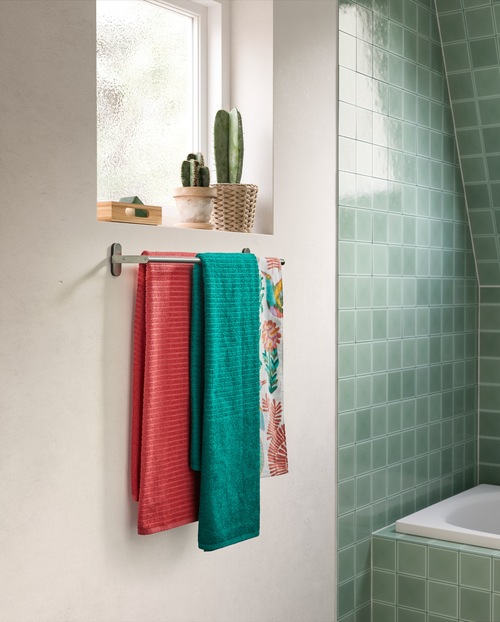 Kamar mandi dengan tema warna merah muda dan turquoise dengan wastafel dan kabinet dinding berwarna putih, keset kamar mandi merah muda, dan tirai shower dengan warna turquoise.