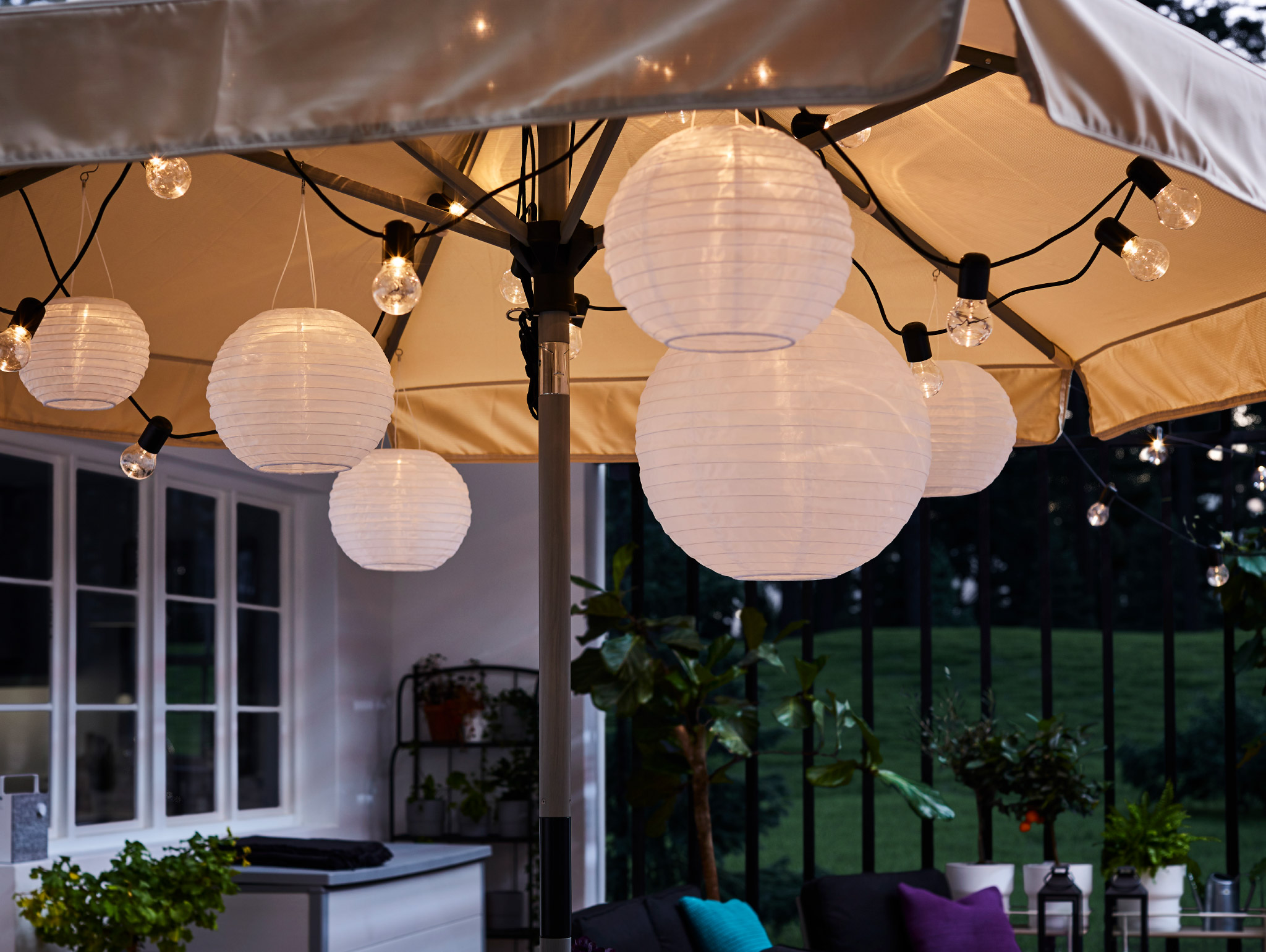 A black lighting chain and round pendant lamps hang under an open parasol, and they give a warm and cosy light.