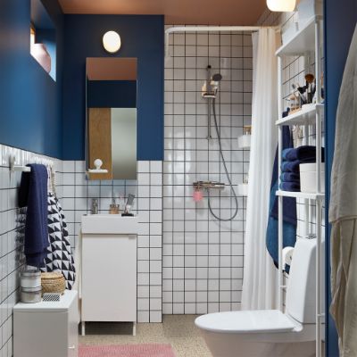 Small bathroom with shower, white furniture, white tiles, dark blue walls, a pink bath mat, a mirror cabinet and blue towels.