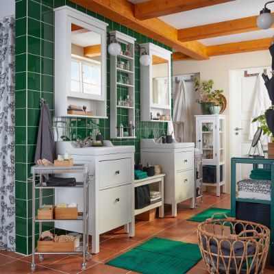 A bathroom with green tiles, two wash-basins, two mirror cabinets, a basket in rattan and two green bath mats.