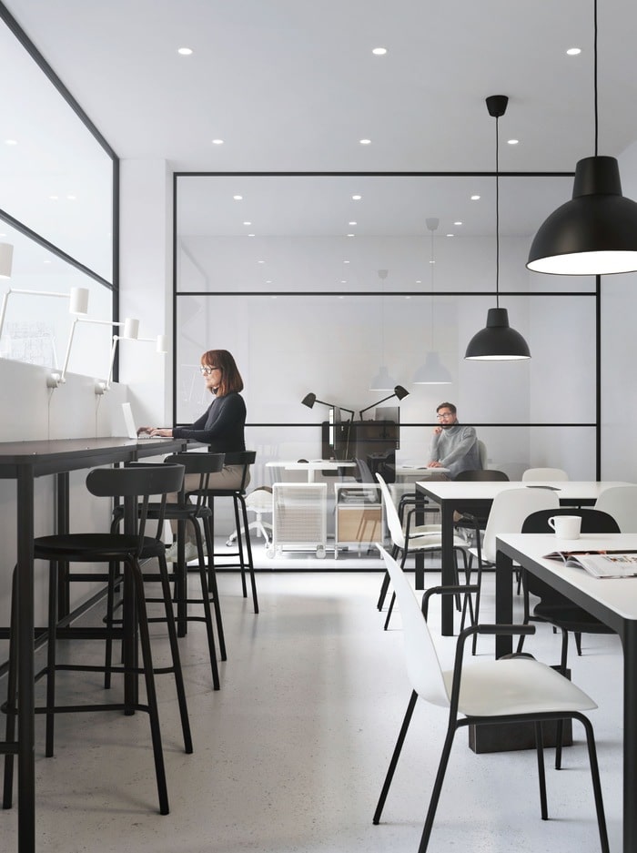 Two work areas – one bar-style with high stools, the other a row of tables. At the back a man is in a glass-fronted office.