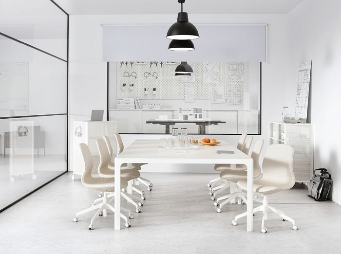 A meeting room with a glass wall containing a large white table. A row of black SKURUP pendant lamps hang from the ceiling.